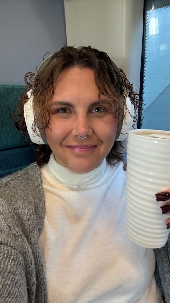 Laura Eccott smiling whilst sitting on a train holding a ceramic reusable coffee mug  