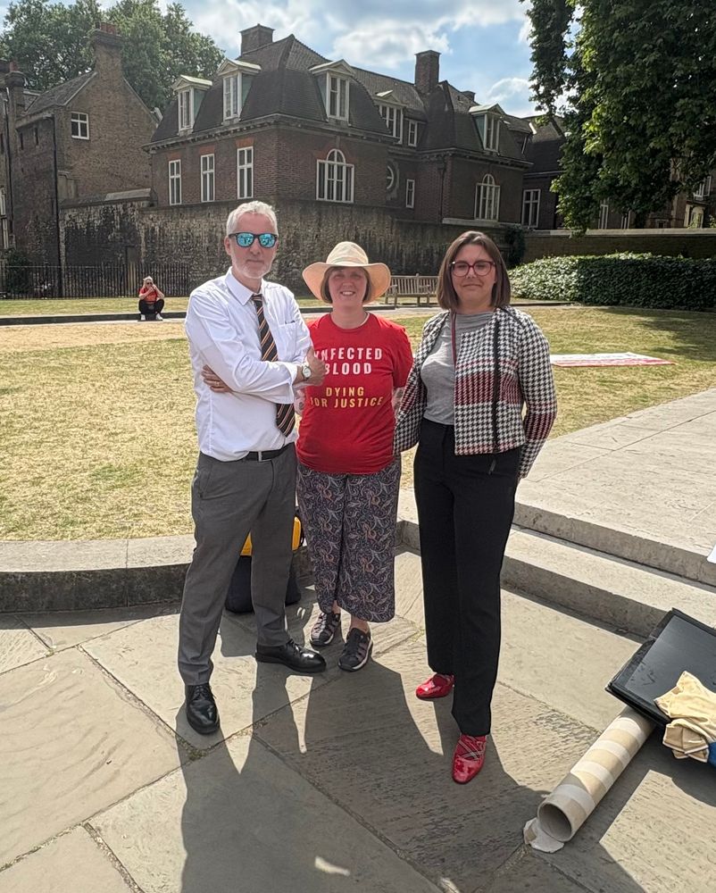 Glenn and Lesley from Contaminated Blood Campaign with Laura Eccott outside
Parliament on a sunny day - t shirt says “infected blood, dying for justice”

