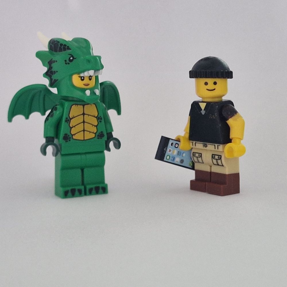 Lego Pete Carrier looks to camera at his side a tall lady in an elaborate green dragon costume. 