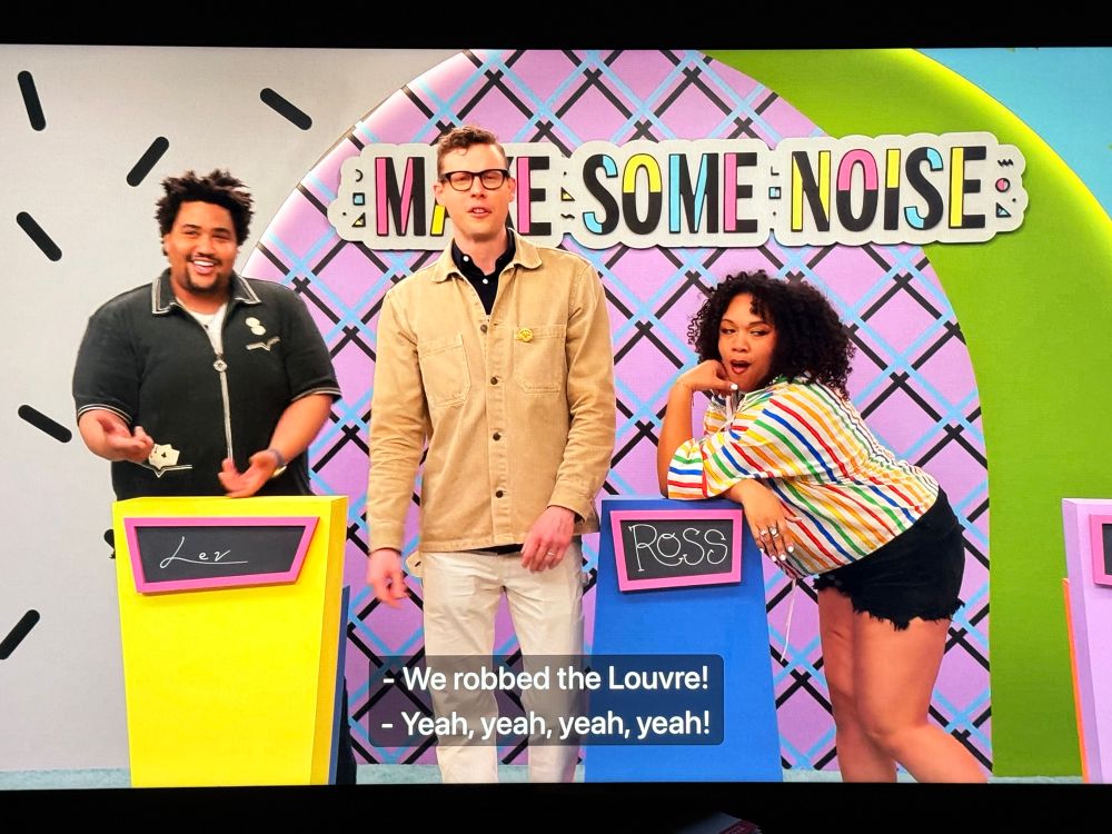 Three folks on a game show, standing at and around their podiums, eye fucking the camera, looking all hot and talented. Closed captioning reads "we robbed the louvre"