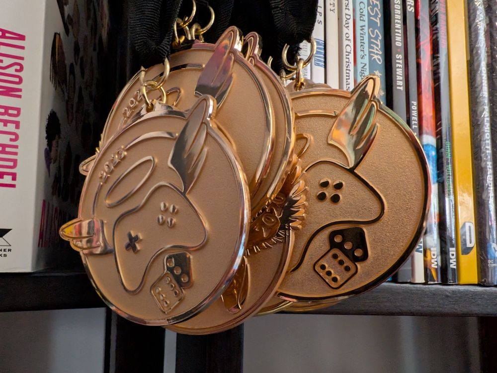 A group of gold medallions featuring a controller emblem with wings and a halo hang on a shelf. Misc. comic books in the background.