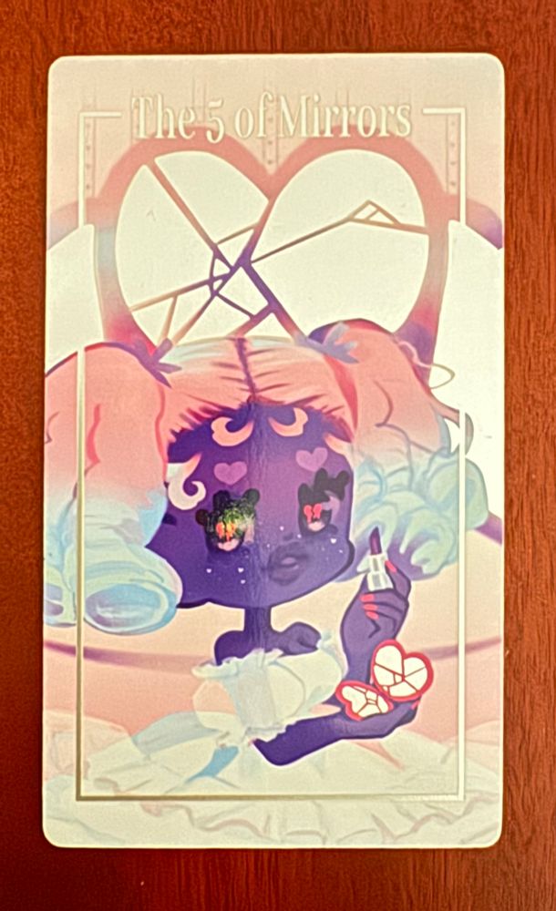 The Five of Mirrors shows a feminine figure with pigtails and purple skin, applying makeup from a heart-shaped compact with cracked glass. The mirror behind her is also cracked. Card by Hexed_Boy.