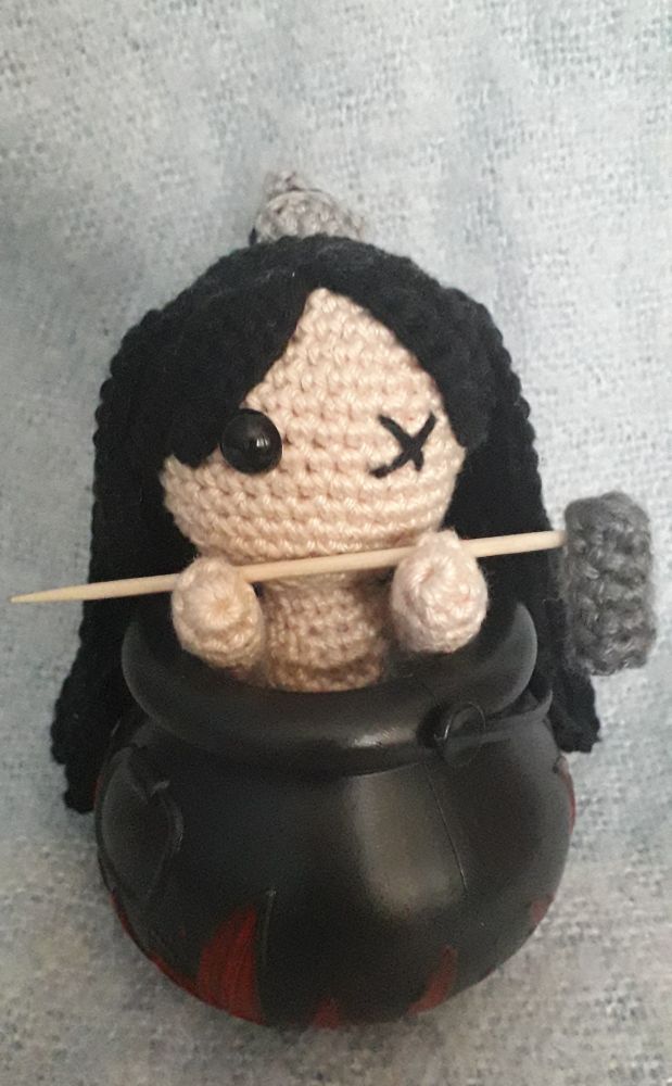 A sj doll with a missing eye sitting in a cauldron with a hammer in his hands 