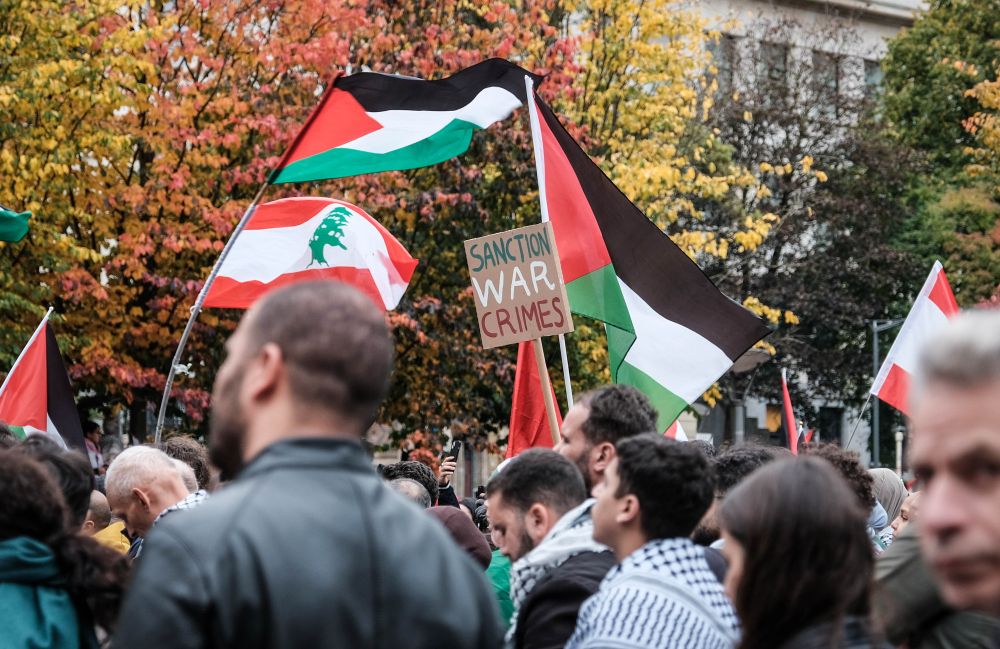 Photo d'une manifestation du 20 octobre 2024 à Bruxelles qui montre des manifestants avec des drapeaux palestiniens et libanais ainsi qu'une pancarte sur laquelle il est écrit "Sanction war crimes". 