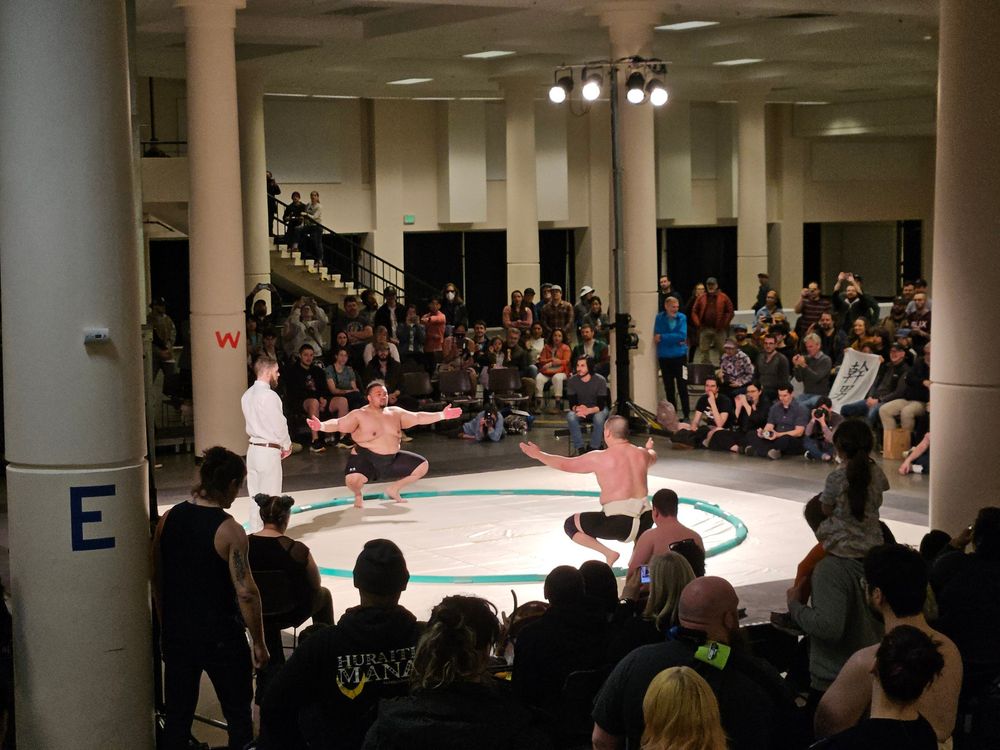 A wide shot of Sua of Rain City Sumo and Niklas of Portland Sumo as they perform chirichozu ahead of their match, while hundreds look on.