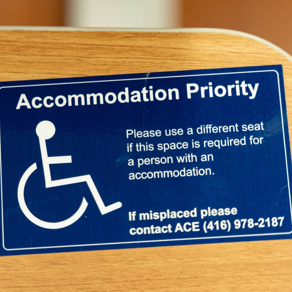 A blue sticker placed on a deck that reads 'Accommodation Priority. Please use a different seat if this space is required for a person with an accommodation.'