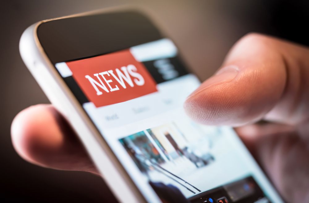 A photo of a hand scrolling through a newsfeed on their phone.