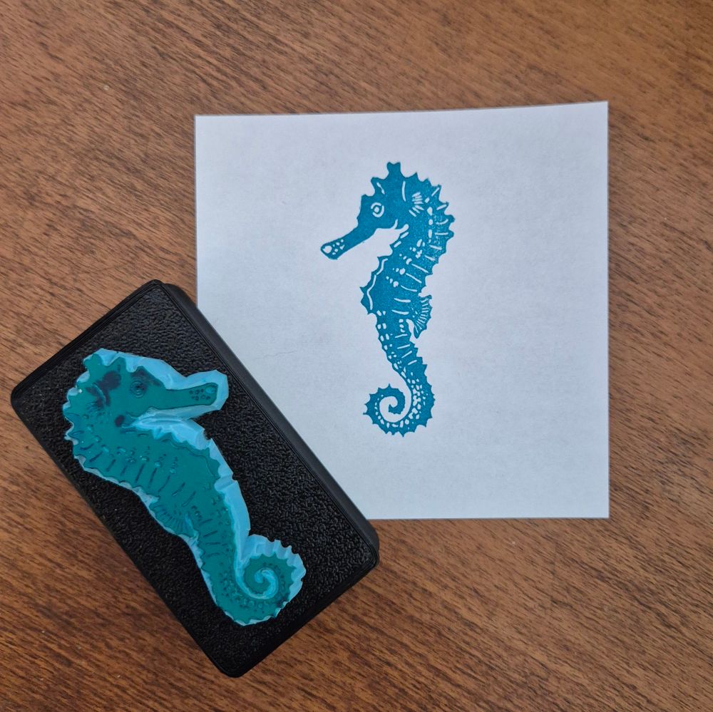 A handcarved rubber stamp and its print in teal. They show a seahorse. 