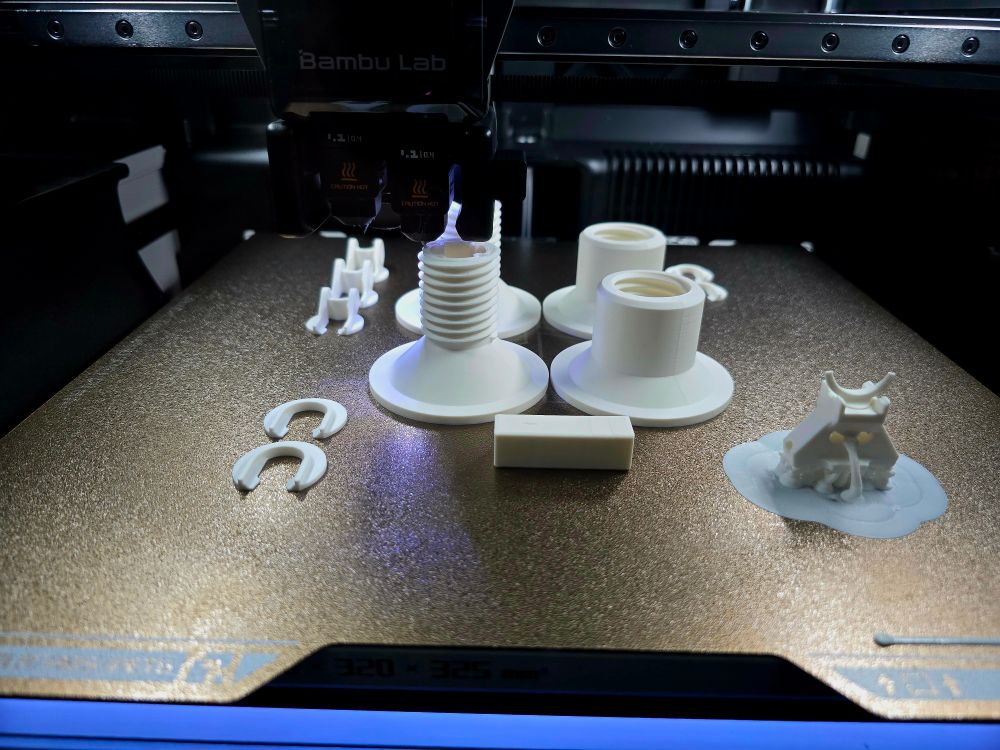 A picture of the inside of a Bambu Lab H2D 3D printer as it is printing various mechanical pieces.