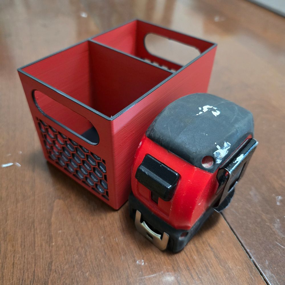 A 3D printed stationery holder inspired by the Milwaukee hardware colors. A Milwaukee tape measure sits on the right.