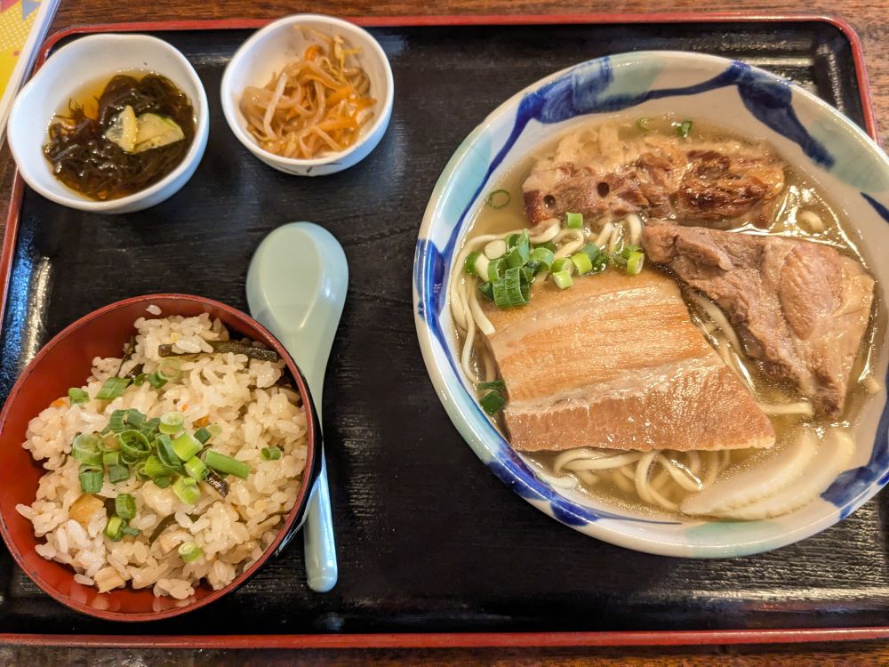 三ツ星まかないそば定食

三ツ星は｢みーちぶし｣と読みます。

三枚肉、軟骨ソーキ、本ソーキの３つが乗っているソーキそばです。お肉の他にもかまぼこが乗っており、小ねぎが散らされています。
定食の内容はジューシー(沖縄の炊き込みご飯)、もずく酢、小鉢(もやしナムル)です。

三枚肉はバラ肉、本ソーキはあばら骨が付いたお肉、軟骨ソーキは軟骨とあばら骨周りのお肉です。本ソーキはあばら骨に比べてやや固めの部位です。どの部位もしっかり味が染みてて美味しいです。バラ肉の肉感も好きですがソーキがめちゃくちゃ美味しいです。特に軟骨ソーキが個人的にぎゅっと美味しさが出てくる感じで良かったです。

麺は中華麺ともそばとも違う変わった感じでコクと深みがあって単体で飲み干せるくらい美味しいスープとよく合います。
これね、ダシが効いてるよダシが。(たぶん)
卓上の七味と紅しょうがの組み合わせは共謀者になる。(謎日本語)
平麺の焼きそばに七味と紅しょうがが合うくらいの良さ！
コーレーグースはちょっと入れるくらいが個人的に好み(途中ちょっと入れすぎちゃった)。ほんのり泡盛感じるか……？？くらいが引き立つのですよ。

ジューシーは沖縄のしっかり味付けの炊き込みご飯で、味濃い地方出身(炊き込みご飯も濃いめ)の私も嬉しい美味しさ。
お野菜と豚？の旨みがご飯に染みてる。
炊き込みご飯おかずに白米行けるヤツだコレ！コメの永久機関！！(大好き)(個人的めちゃくちゃ褒め言葉)

小鉢にもやしナムル(サッパリで良いよね)は見かけますがもずく酢はなかなか見ないかも。なんかラッキー。
あまり普段食べなくてもずくに対する解像度低いから半分飲むみたいな印象だったけどしっかり''食べる''なもずくで美味しかったです。
主食系に対するさっぱり系の小鉢、暑い日だったのもあって嬉しい。

沖縄そばにソーキが入っていたらソーキそばらしいですね。
1口目の汁でこれもはやソーキ無くても…？とか思うくらい好みの味でした。…が、美味しさ加速装置と思うくらいお肉達と麺＆スープの相性が良くて旨みがこぼれてくるような感じでした。ある意味2種類のスープを楽しめるソーキ必要だなコレ！！！！
スープ冷たいのと暖かいの、季節に合わせて水筒とか魔法瓶に入れて持ち運びたい。