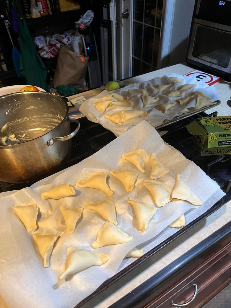 Photo of two baking sheets covered in layers of pierogi on wax paper. 