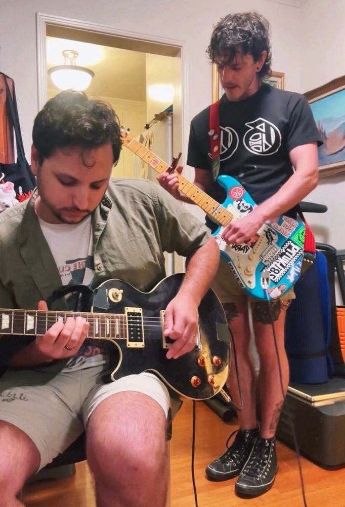Photo of Kasey + James playing their guitars during rehearsal. James is seated + Kasey stands behind him. 🖤 SH!NER is a queer alternative band in LA