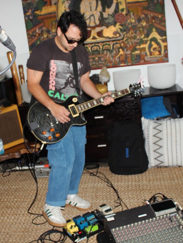 James standing at his pedal board + tuning his guitar during rehearsal 