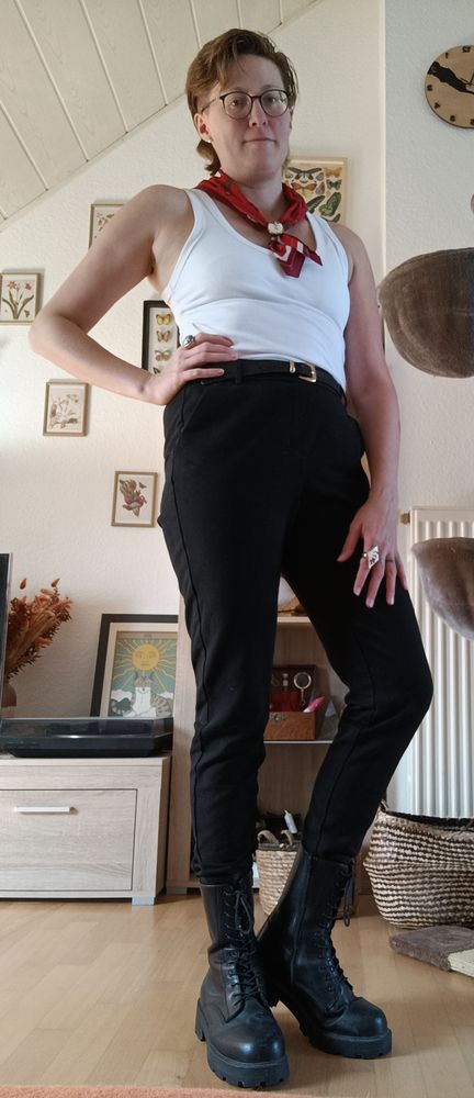 Outfit inspiriert von der Figur Orpheus aus dem Musical Hadestown. Schwarze Boots, schwarze Stoffhose, schwarzer Gürtel mit goldener Schnalle, weißes Tanktop, rotes Bandana als Handtuch um den Hals.