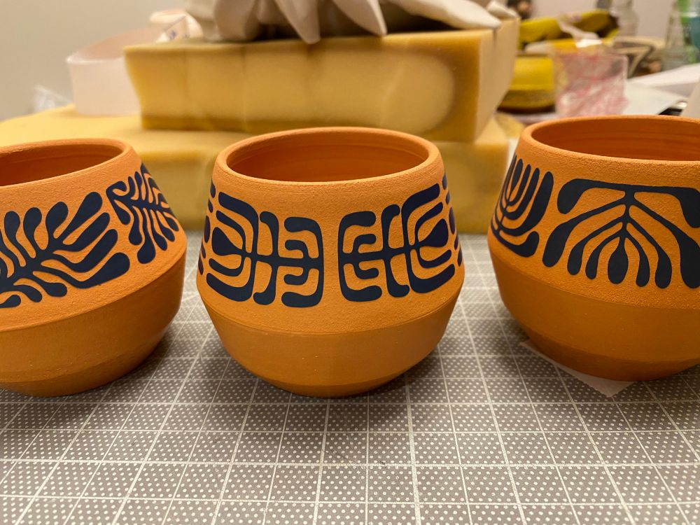 Three bisqued red clay cups with vinyl stencil attached on the upper portion in repeating patterns