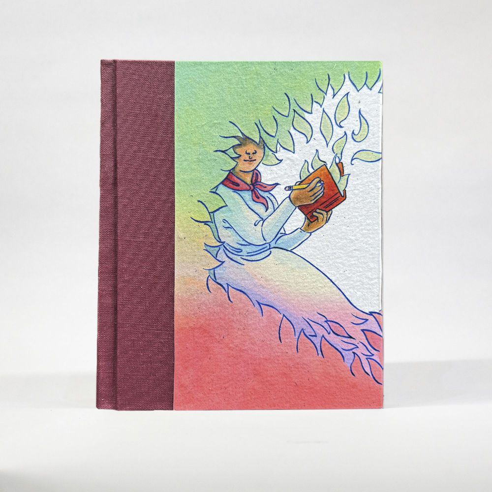 A notebook with the cover visible stands on a white background. The spine is a burgundy wine color, with a natural white, textured, handmade paper cover featuring a design in muted green, rose pink, and blue of a woman sitting among leaves with a journal in her hand.