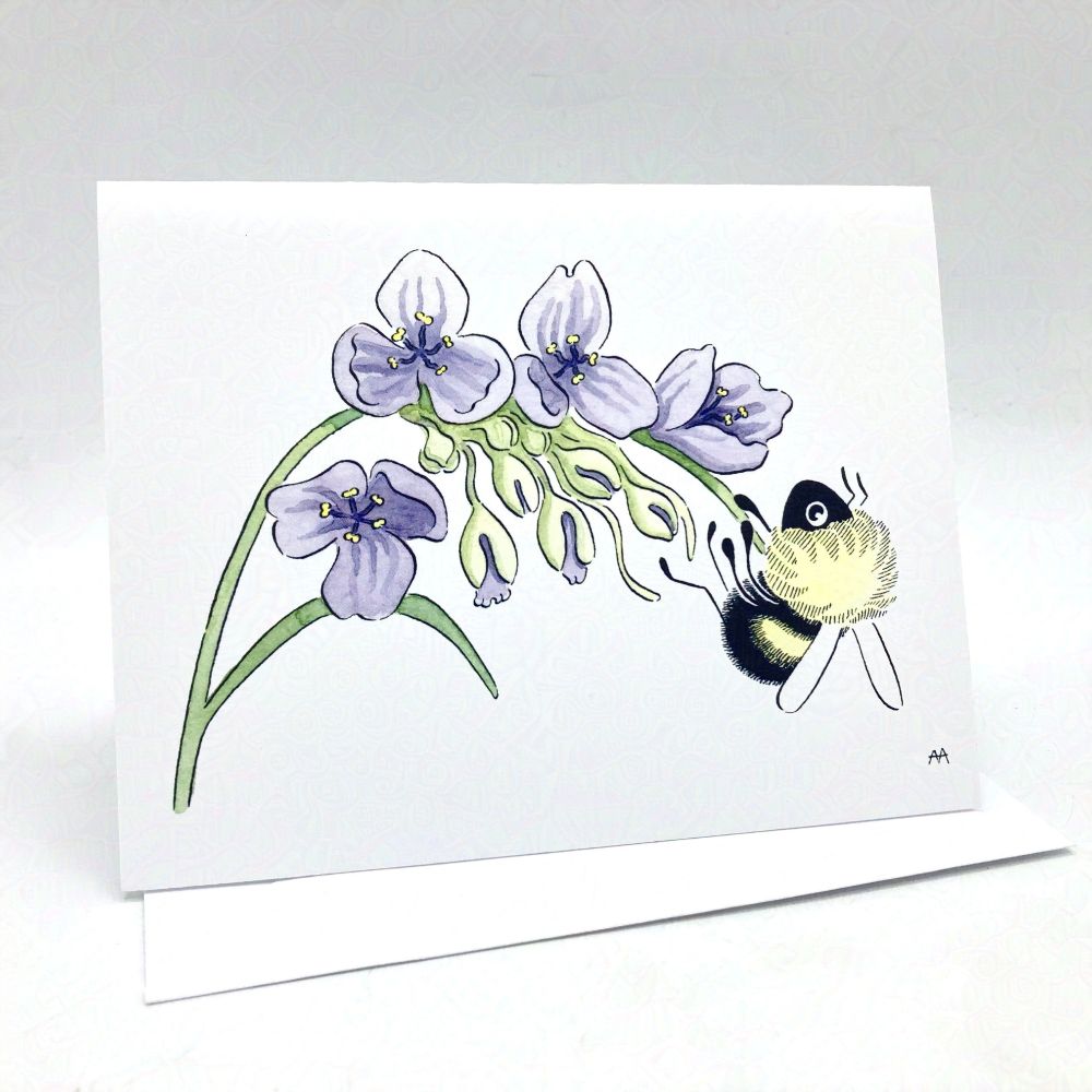 A notecard placed on a white envelope in a white background. Notecard shows an ink and watercolor design of a fuzzy bumblebee handing onto the leaf of a ohio spiderwort plant, with green buds and four purple flowers present.