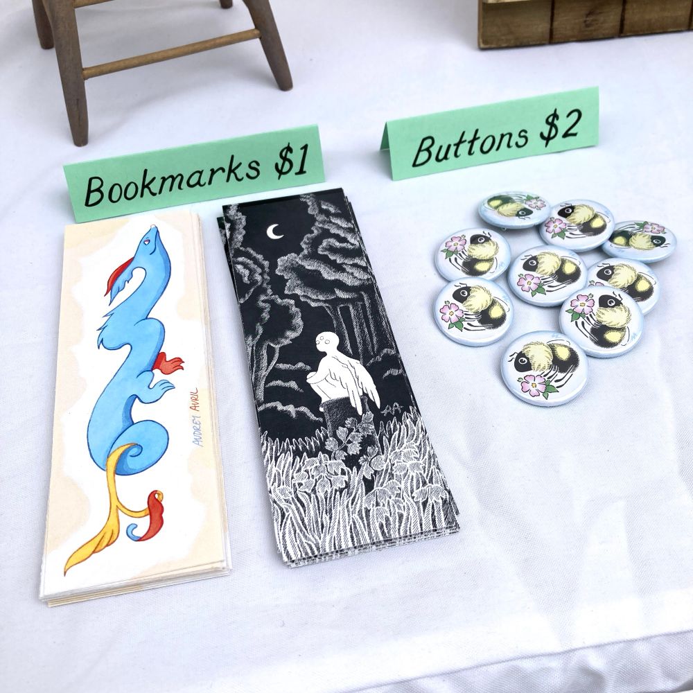 A photograph featuring pinback buttons with a bumblebee design and two ink and watercolor bookmark designs.