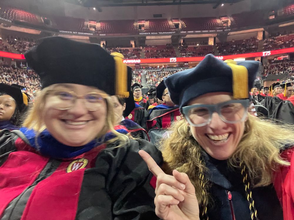 Two blonde ladies in regalia grinning their faces off. Kohl Center beyond.