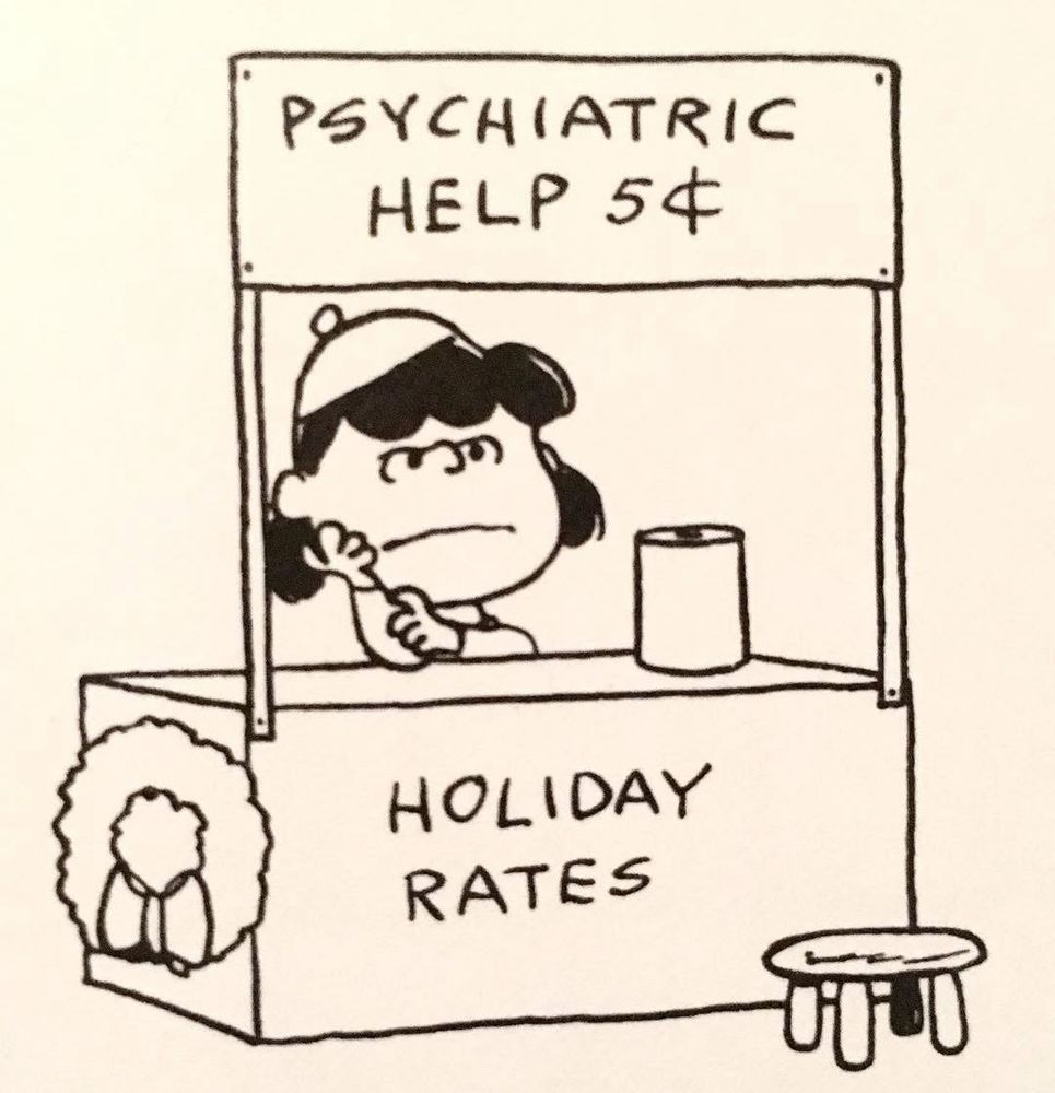 Lucy from Peanuts sitting at her Psychiatric Help booth which is decorated with a wreath. She has a crabby expression. The front of the booth reads “Holiday Rates.”