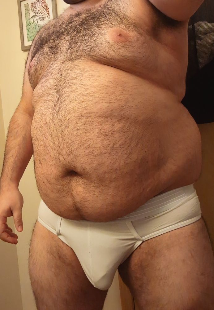 A photo of me in a pair of white briefs and nothing else. There's a low hanging bulge in the center of my underwear. 