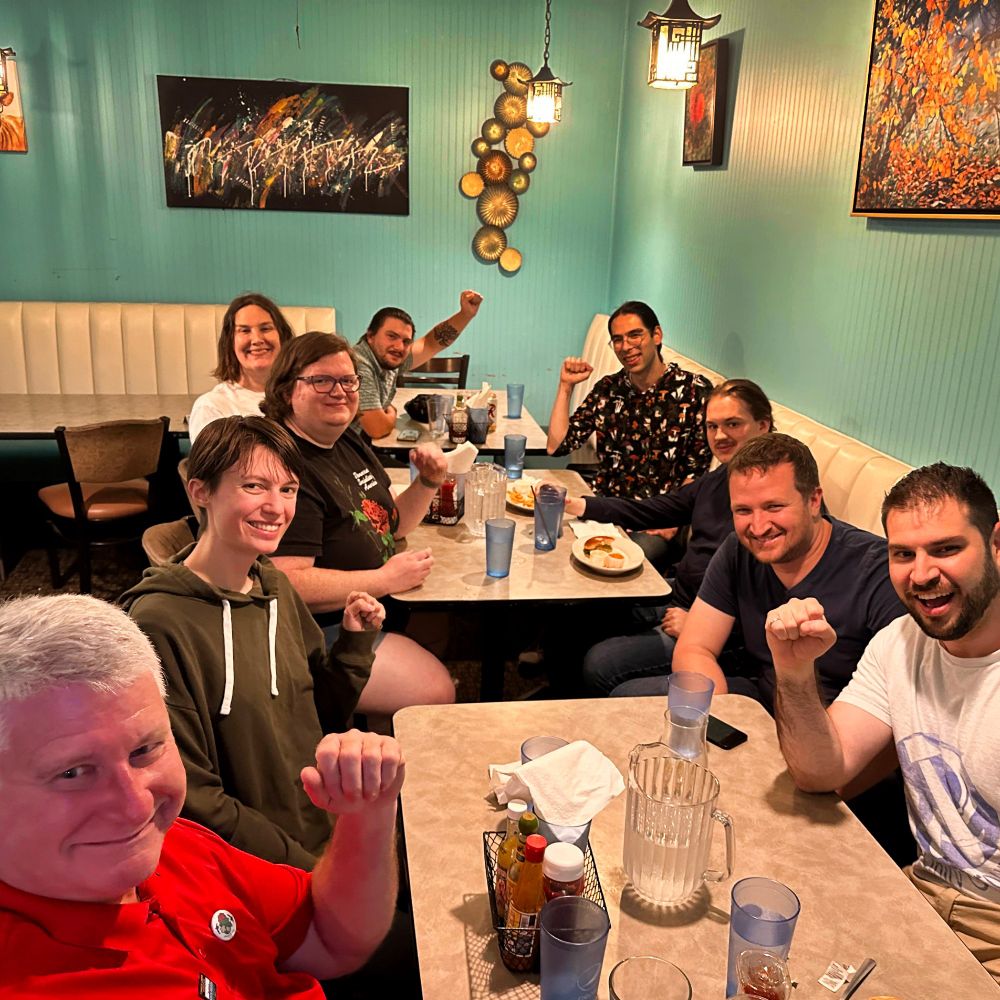 Several SnoCo DSA members sit with Amy from the DSA National Political Committee. They are raising their fists in solidarity and smiling for the camera.