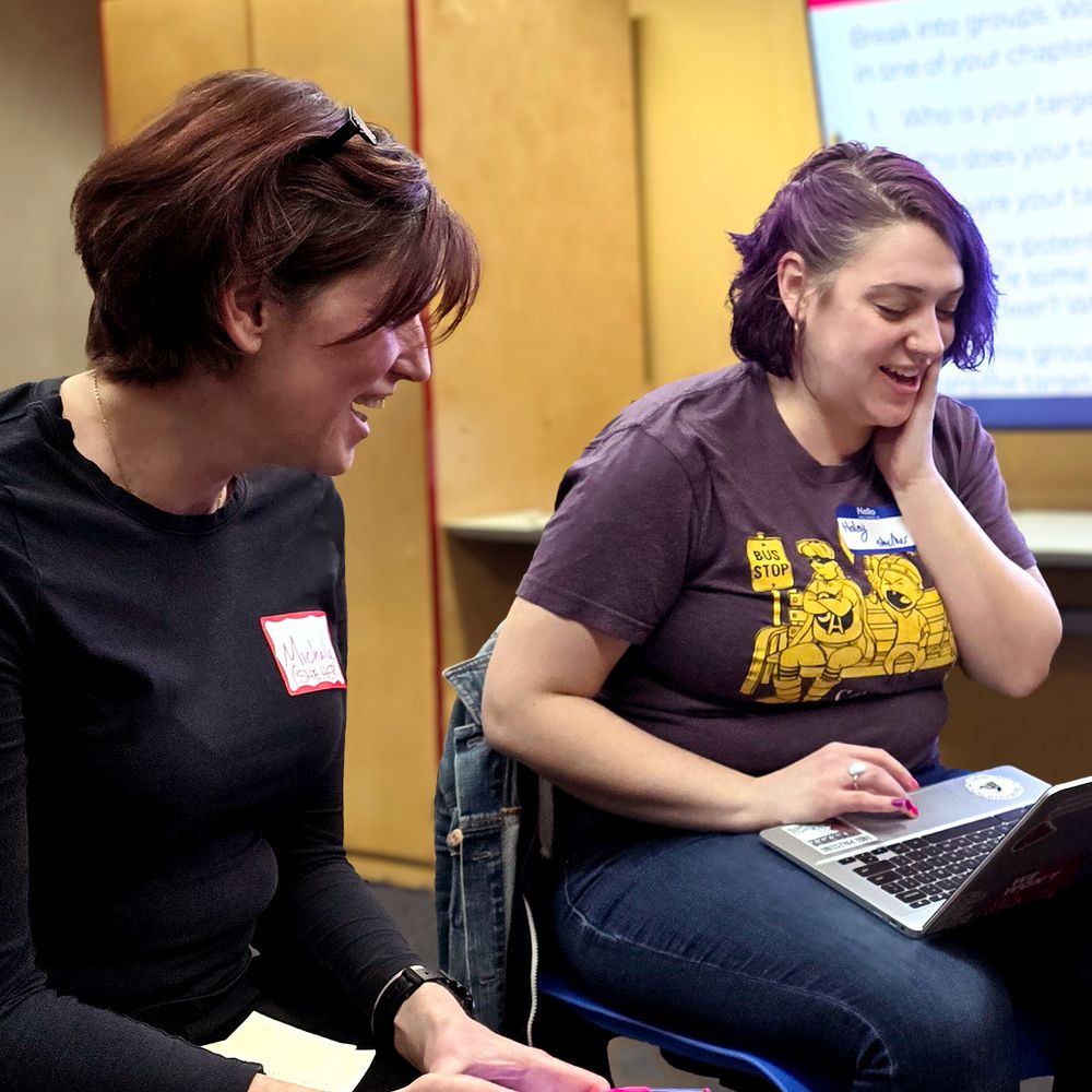 Two SnoCo DSA members sit in a classroom, laughing together as they work on a project.
