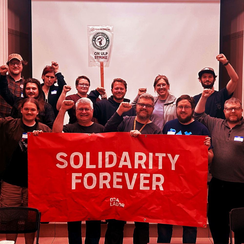 Several SnoCo DSA members at a Labor & Strike Working Group meeting pose together with solidarity fists raised and a banner that says "Solidarity Forever - DSA Labor"