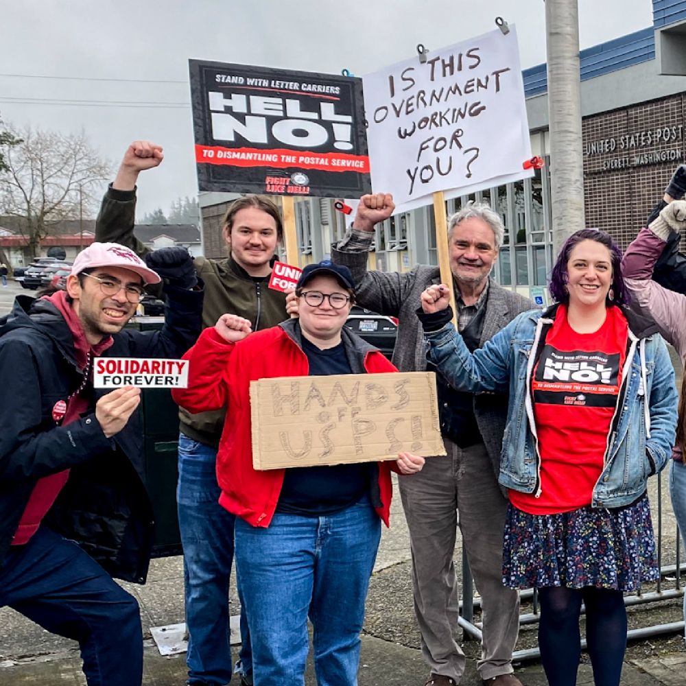 Several SnoCo DSA members pose for a photo with fists raised in solidarity at a "Stand with Letter Carriers" event earlier this year (2025).