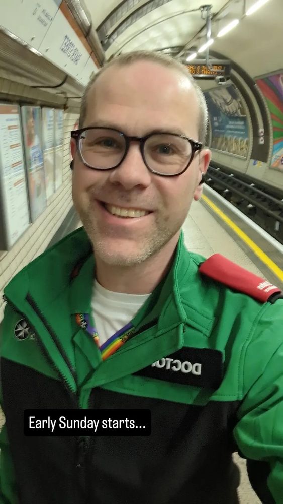 Smiling doctor in glasses and green/black St John Ambulance uniform on the platform of Baker Street tube station