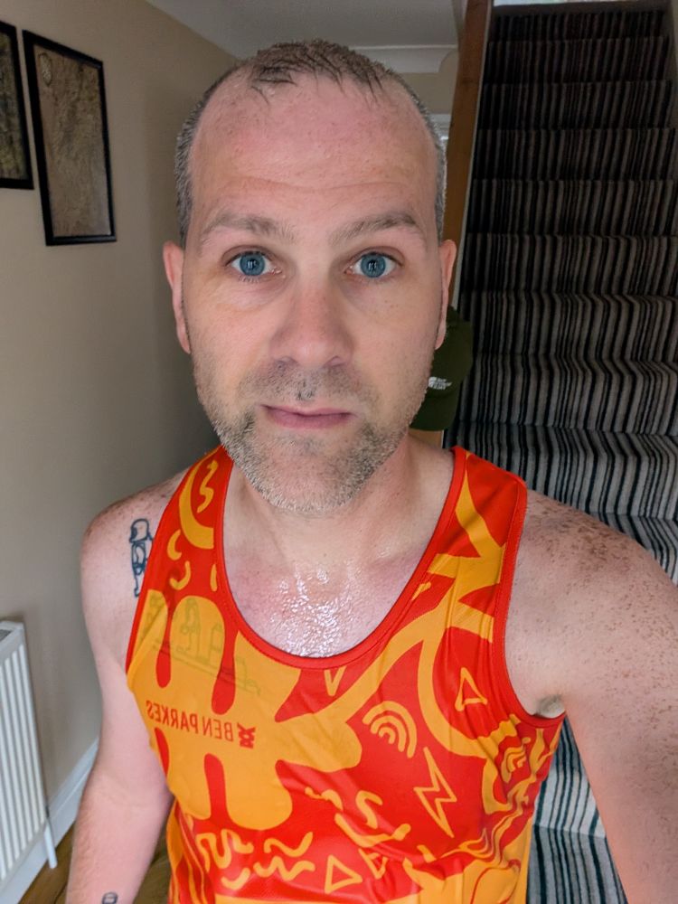 Selfie: Me in an orange running vest looking directly at the camera with a relatively neutral expression while soaked to the skin 