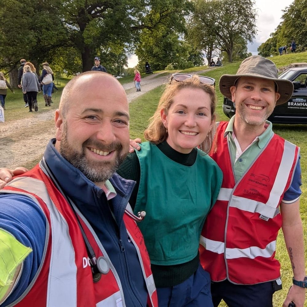 Group of smiling people at the end of a long day of volunteering - two men in red hi-vis vests flanking a woman in a green vest 