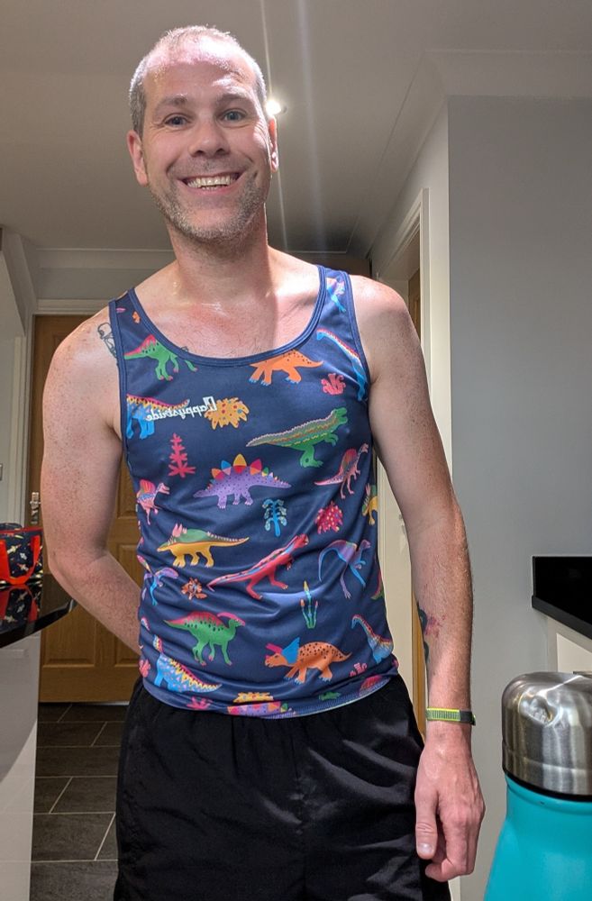 Smiling man in running shorts and vest - the vest is blue and covered with cartoon dinosaurs 