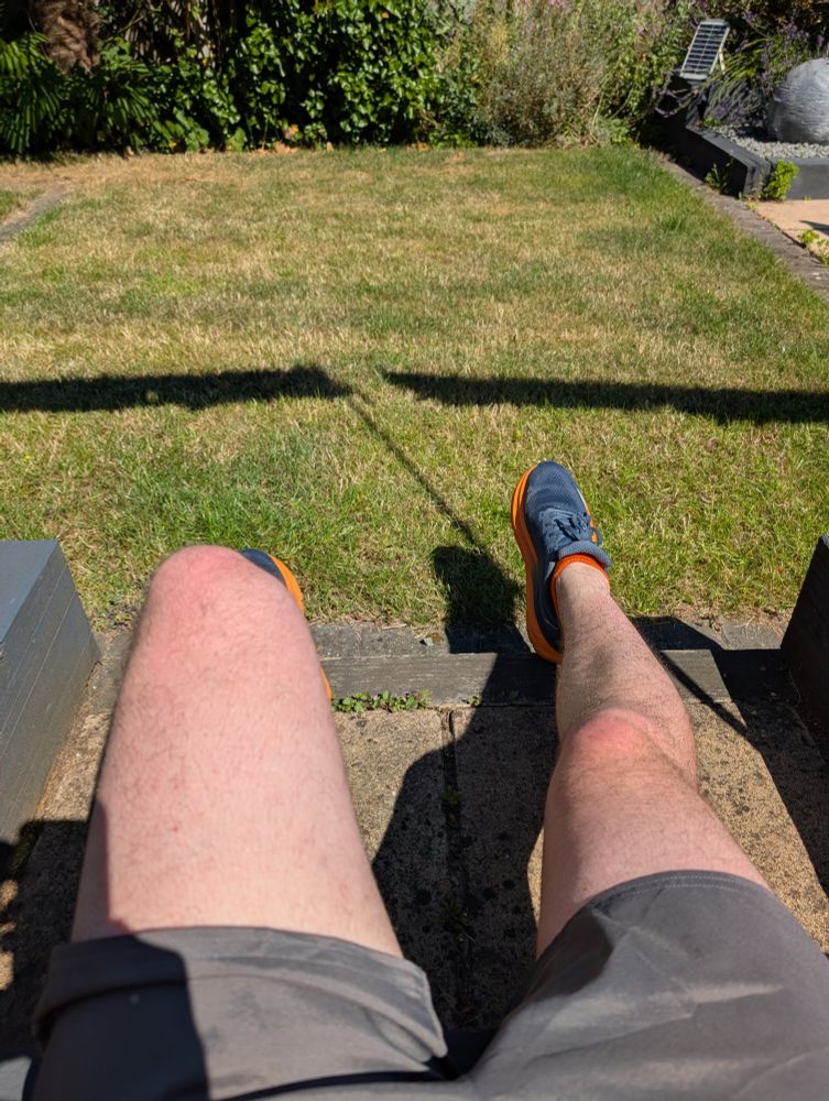 Sitting on the step in the back garden in grey shorts and running trainers - only my legs are visible in the image with the garden in the background