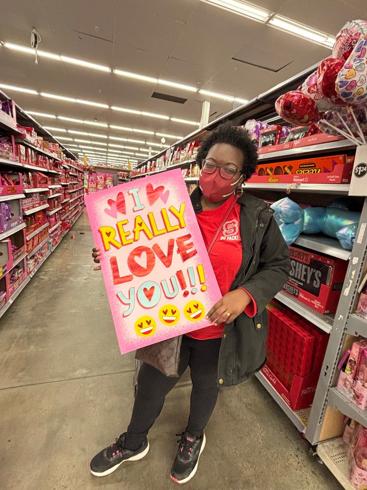 Jasmine wearing a red KN95 mask while holding a large Valentine’s Day card
