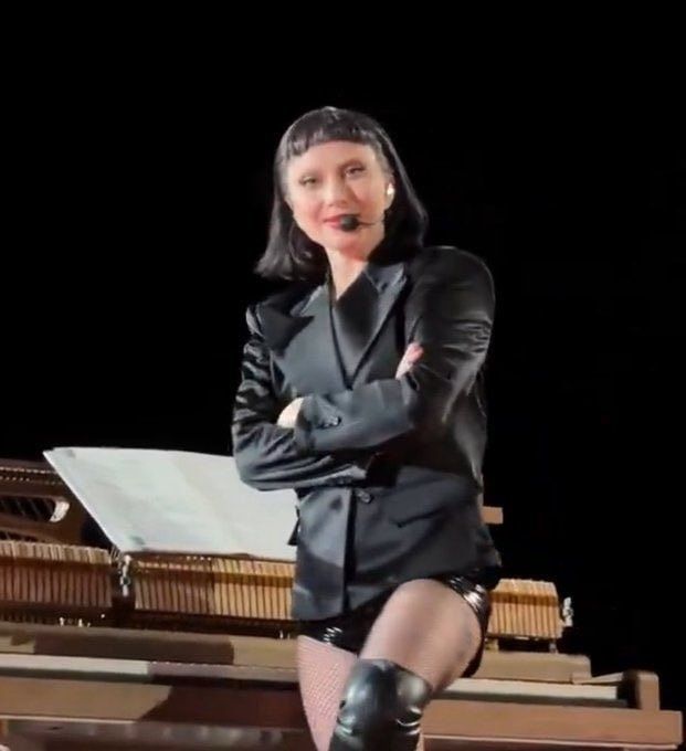 lady gaga em pé e de braços cruzados olhando pra frente com um sorriso um tanto incrédulo 