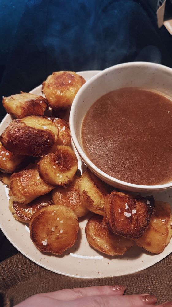 A plate of crispy roast potatoes with a big bowl of gravy on the side