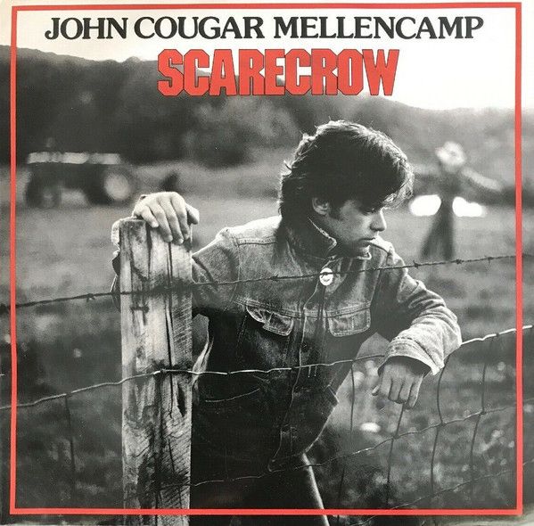 Black and white photo of John Mellencamp leaning on barbed wire fence. Scarecrow title in red. 
