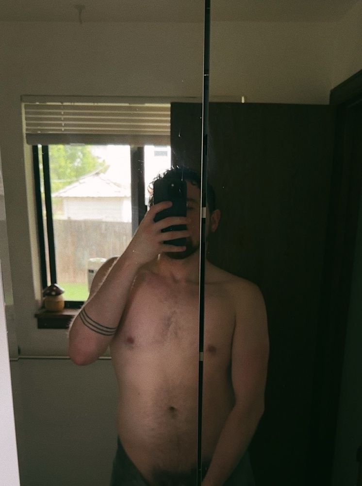 Mirror selfie of a shirtless man with a towel loosely wrapped around his waist