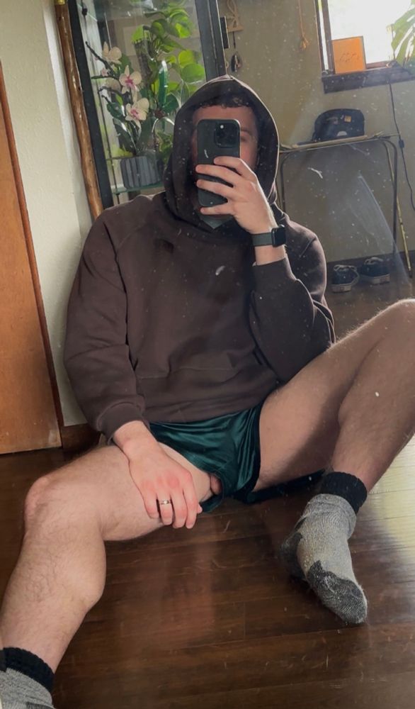 Man wearing hoodie with hood up and satin boxers sitting in front of a mirror