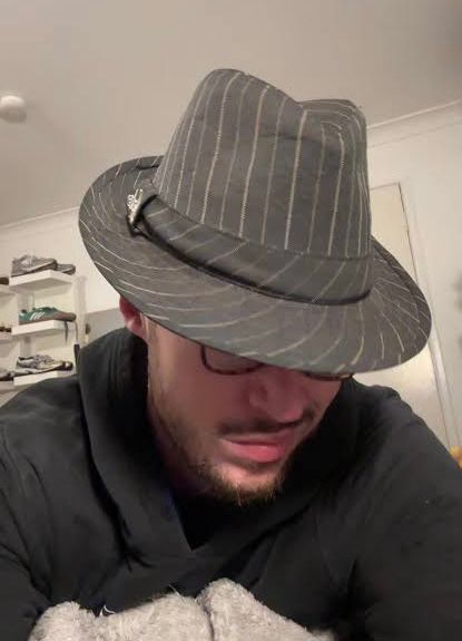 Man wearing a fedora that is obscuring his face except for his smirk