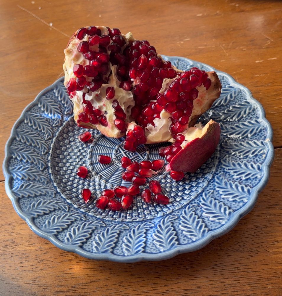 An opened pomegranate spilling ruby red seeds onto a cornflower blue plate 