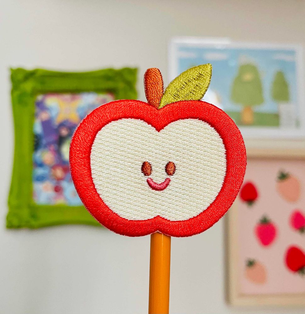 an embroidered patch of a smiling sliced apple. 