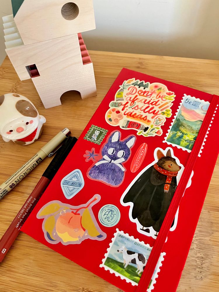 a bright red sketchbook covered in stickers that have a colorful, rustic feel. 