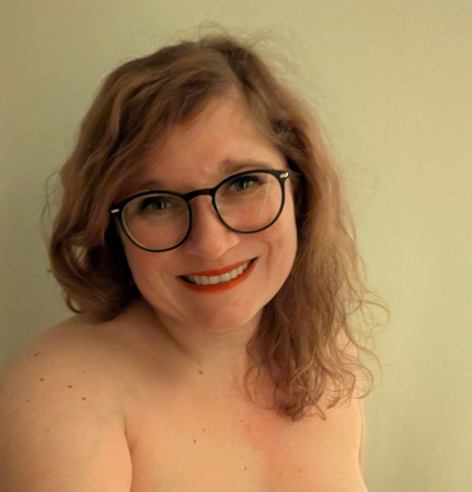 Selfie.Ich lächle in die Kamera. Offene wellige blonde Haare, Lidstrich & Mascara, Grüße schwarze Brille mit goldenen Applikationen. Roter Lippenstift. Und ich bin dabei Oberkörperfrei. Man sieht mich bis zum Dekolleté. 