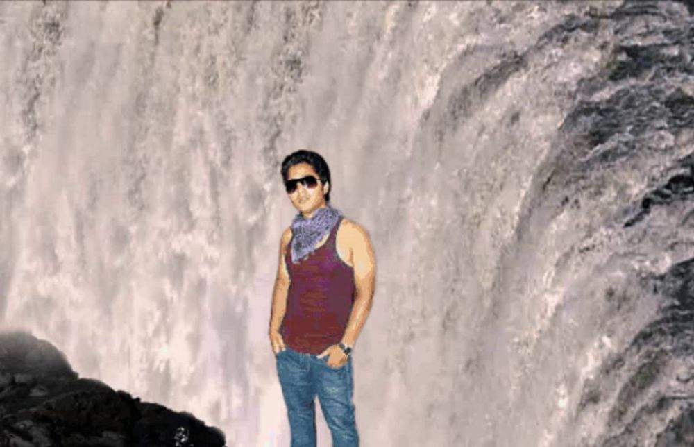 a man wearing sunglasses and a red tank top stands in front of a waterfall