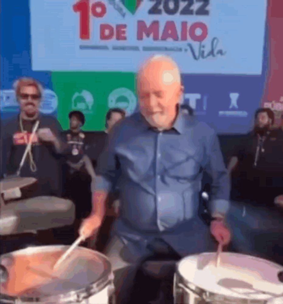 a man playing drums in front of a sign that says 1o de maio