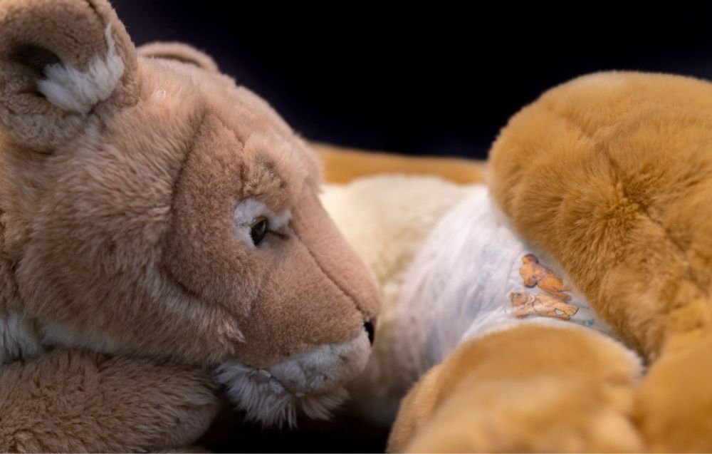 Plush lioness is sniffing at an other plush lioness diaper.