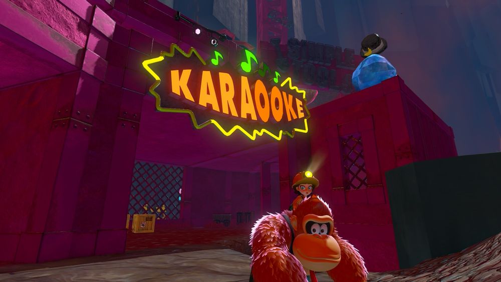 Screenshot from Donkey Kong Bananza. DK and Pauline (who is wearing a miners helmet with a lit light on it) stand in front of a half-lit sign which reads “Karaooke” cause monkeys. Quiztone is tipping his hat away from the camera in the background .